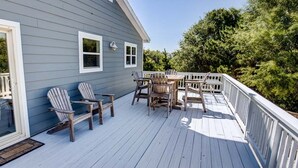 Une terrasse en bois, agrémentée de chaises Adirondack et d’une table, le tout entouré d’une rambarde blanche.