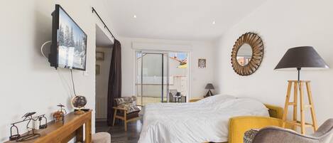 A bedroom with a bed, a desk, a chair, a lamp, and a television.