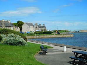 A waterfront promenade with benches, a stone wall, and buildings in the background. - Welcomehouse is a lovely bungalow close to the beach with FREE WIFI. (Lossiemouth)