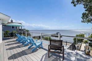 A deck with blue chairs and a table, overlooking a body of water with a dock and pier. - Bella Sound | Sound Front | Community Pool, Hot Tub | Duck (Duck)