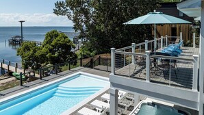 Ett poolområde med en bubbelpool, solstolar och utsikt över vattnet.