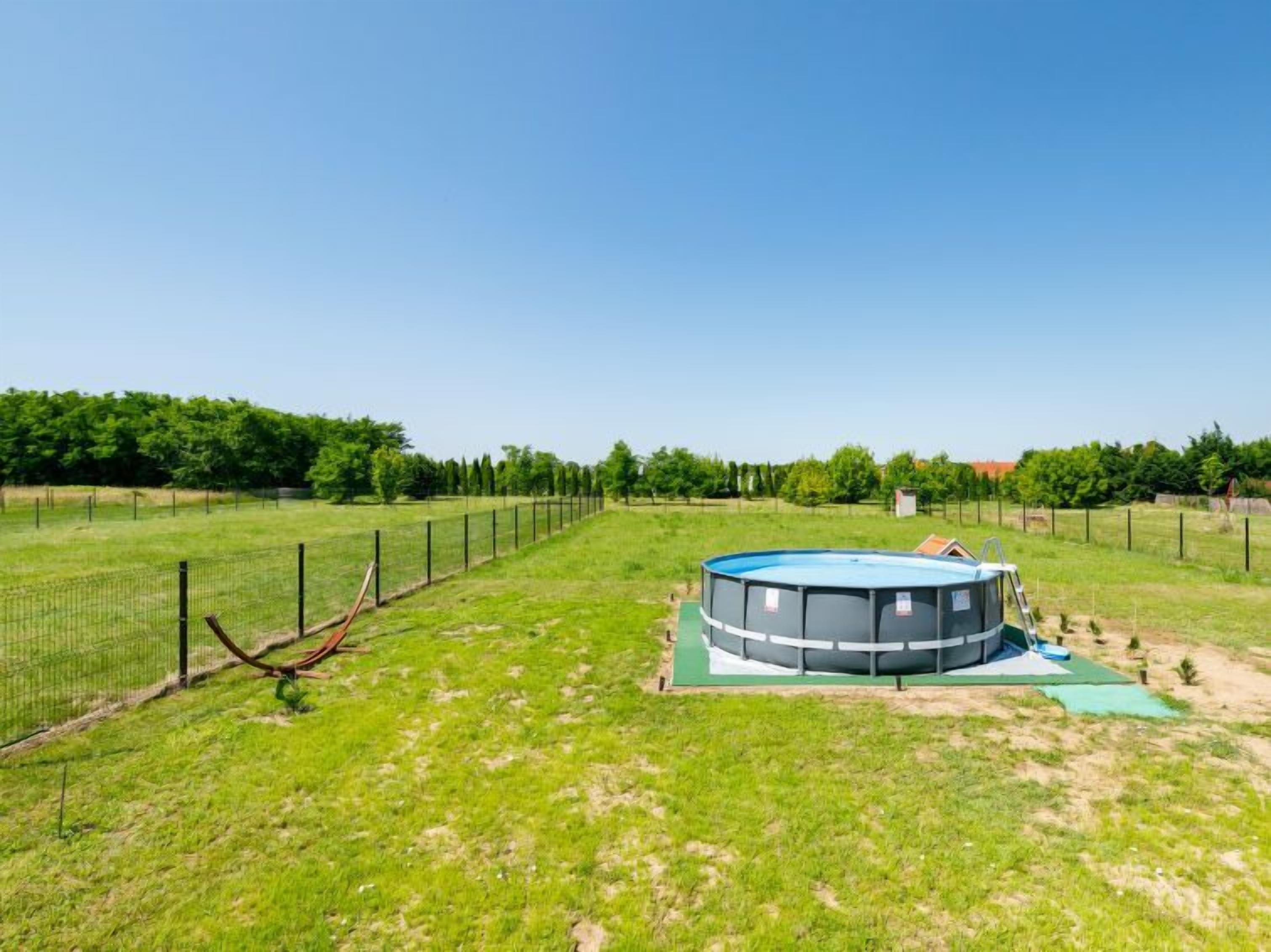 A circular building with a blue roof, surrounded by a fenced area with green grass and trees in the background.