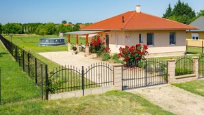 Ein eingeschossiges Haus mit rotem Dach, einer überdachten Terrasse und einem eingezäunten Garten.