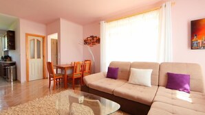 Ein Wohnzimmer mit einem beigefarbenen Sofa, einem Glastisch und einem Essbereich mit Holztischen und einem Tisch.