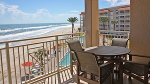 Un balcon avec vue sur la plage et l’océan, équipé d’une piscine, de chaises et de parasols.