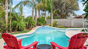 A swimming pool with red chairs and a table, surrounded by palm trees and a brick wall. - Gilbert Home, Walk to Downtown, Restaurants, Nightlife 10+ location! (Gilbert)