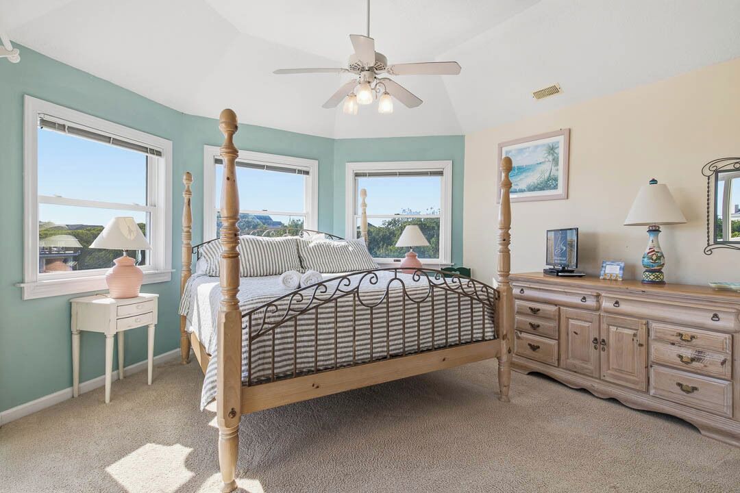 A bedroom with a four-poster bed, a ceiling fan, a dresser, and a window with a view.
