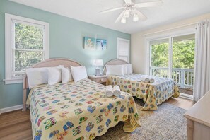 A bedroom with two beds, a ceiling fan, and a large window with a view of trees.
