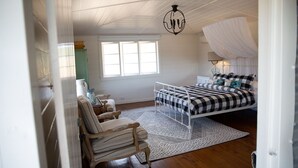 Un dormitorio con cama, una silla, un ventanal y una araña.