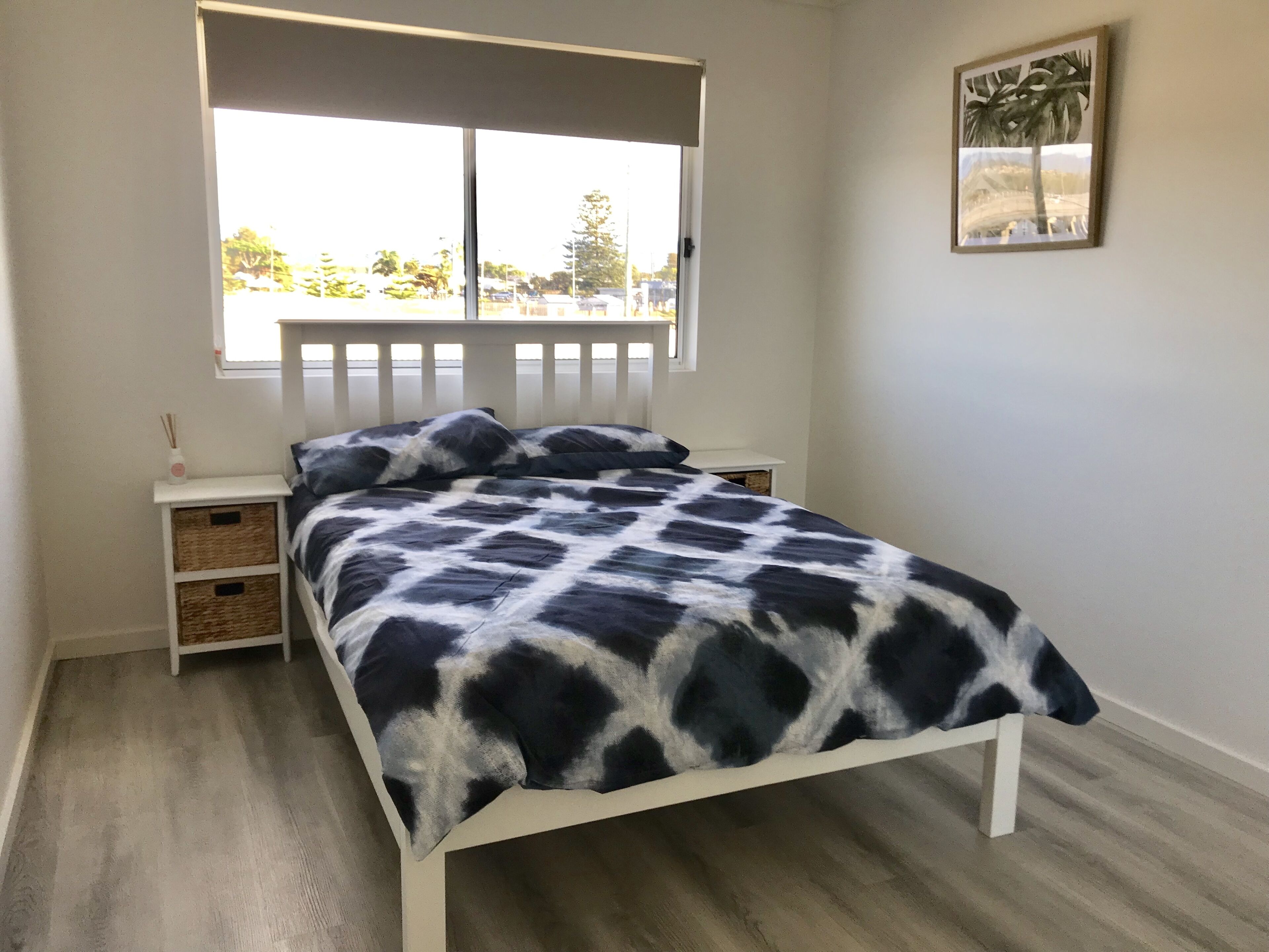 A bedroom with a bed, a nightstand, a window, and a wall-mounted picture.