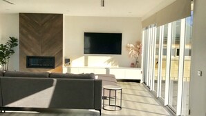A modern living room with a large flat-screen TV, a sofa, and a small round table. - The Lakehouse Windang (Windang)