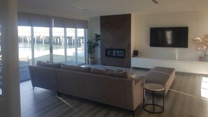 A modern living room with a large sofa, a flat-screen TV mounted on the wall, and a view of a waterfront through large windows. - The Lakehouse Windang (Windang)