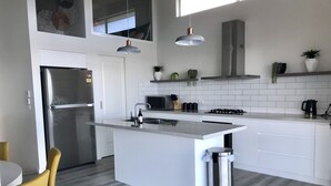 A modern kitchen with a central island, stainless steel appliances, and a grey tiled backsplash. - The Lakehouse Windang (Windang)