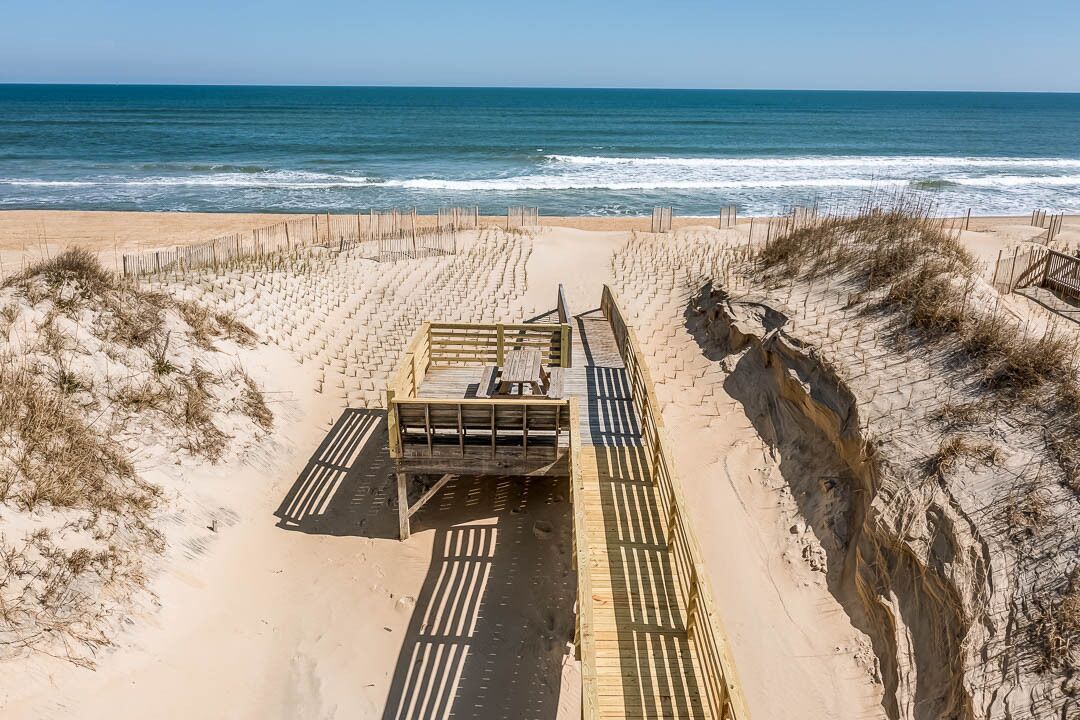 Une plage avec une promenade en bois menant à une entrée fermée par un portail.