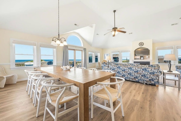 A spacious dining area with a wooden table and white chairs, a patterned sofa, and a view of the ocean.