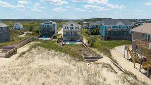 A coastal residential area with houses, a sandy beach, and a wooden boardwalk. - Glistening Sands | Oceanfront | Private Pool, Hot Tub | Nags Head (Nags Head)