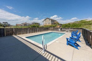 Ein Swimmingpool mit Holzterrasse, blauen Liegestühlen und einem Gebäude im Hintergrund.