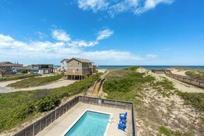 A beachfront property with a swimming pool, beach access, and a large house with multiple levels.