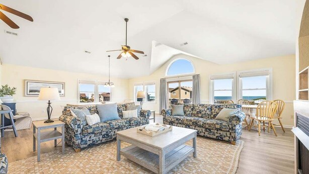 A spacious living room with two patterned sofas, a coffee table, and a ceiling fan. - Glistening Sands | Oceanfront | Private Pool, Hot Tub | Nags Head (Nags Head)