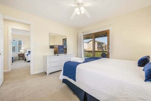 A bedroom with a large bed, a dresser, a mirror, and a balcony with a view.