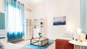 A modern living room with a sofa, a coffee table, a bookshelf, a painting, and a lamp.