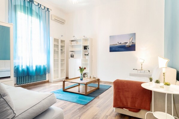 A modern living room with a sofa, a coffee table, a bookshelf, a painting, and a lamp.