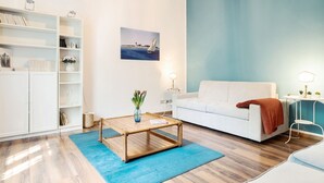A modern living room with a white sofa, a coffee table, a bookshelf, and a painting of a sailboat.