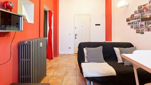 Een kamer met een zwarte bank, een witte tafel, een radiator, een rood gordijn en een deur.