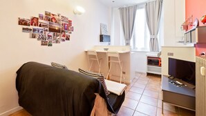Een compacte kamer met een bed, een kleine kitchenette, een eethoek en een wand versierd met foto's.