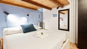 Een slaapkamer met een houten plafond, een bed met witte lakens, een blauw kussen en een spiegel aan de muur.