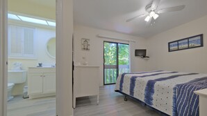 A bedroom with a bed, a ceiling fan, a TV, and a sliding glass door to a balcony.