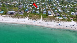 An aerial view of a coastal residential area with houses, a beach, and clear turquoise waters.