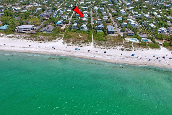 An aerial view of a coastal residential area with houses, a beach, and clear turquoise waters.