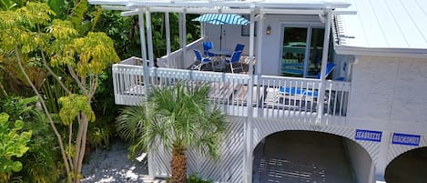 Eine überdachte Terrasse im Freien mit blauen Stühlen und einem Tisch, umgeben von üppiger Vegetation und einer Palme.