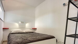 Ein modernes Schlafzimmer mit einem Bett, einem roten Regal, einem weißen Kopfteil und einem schwarzen Metallregal.