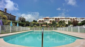 Ein Swimmingpool mit weißem Zaun, umgeben von einem weißen Gebäude mit mehreren Balkonen und einem strahlend blauen Himmel.