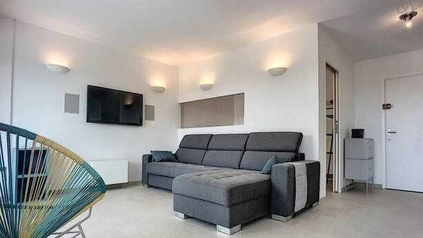 Ein modernes Wohnzimmer mit grauem Sofa, einem farbenfrohen Sessel, einem flachbildfernseher an der Wand und Einbauschränken.