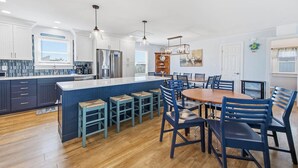 Uma cozinha moderna com uma ilha central, banquetas de bar e uma mesa de jantar com cadeiras.