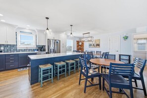 A modern kitchen with a central island, bar stools, and a dining table with chairs.