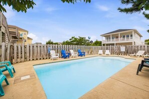 A swimming pool with lounge chairs, a wooden fence, and a two-story building in the background.