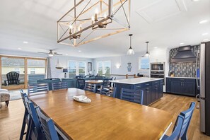 A modern kitchen with a central island, dining area with blue chairs, and a large wooden table.