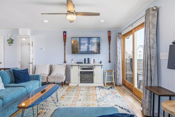 A living room with a sofa, coffee table, fireplace, and a view through a glass door. - Sea Scapes | 817 ft from the beach | Private Pool, Hot Tub | Corolla (Corolla)