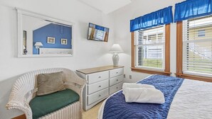 Quarto com cama, poltrona, cômoda e janela com persianas.