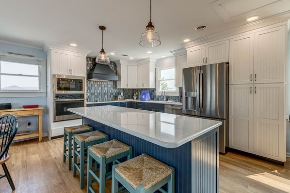 Una cocina moderna con una isla grande, armarios blancos, electrodomésticos de acero inoxidable y una zona de asientos tipo bar.