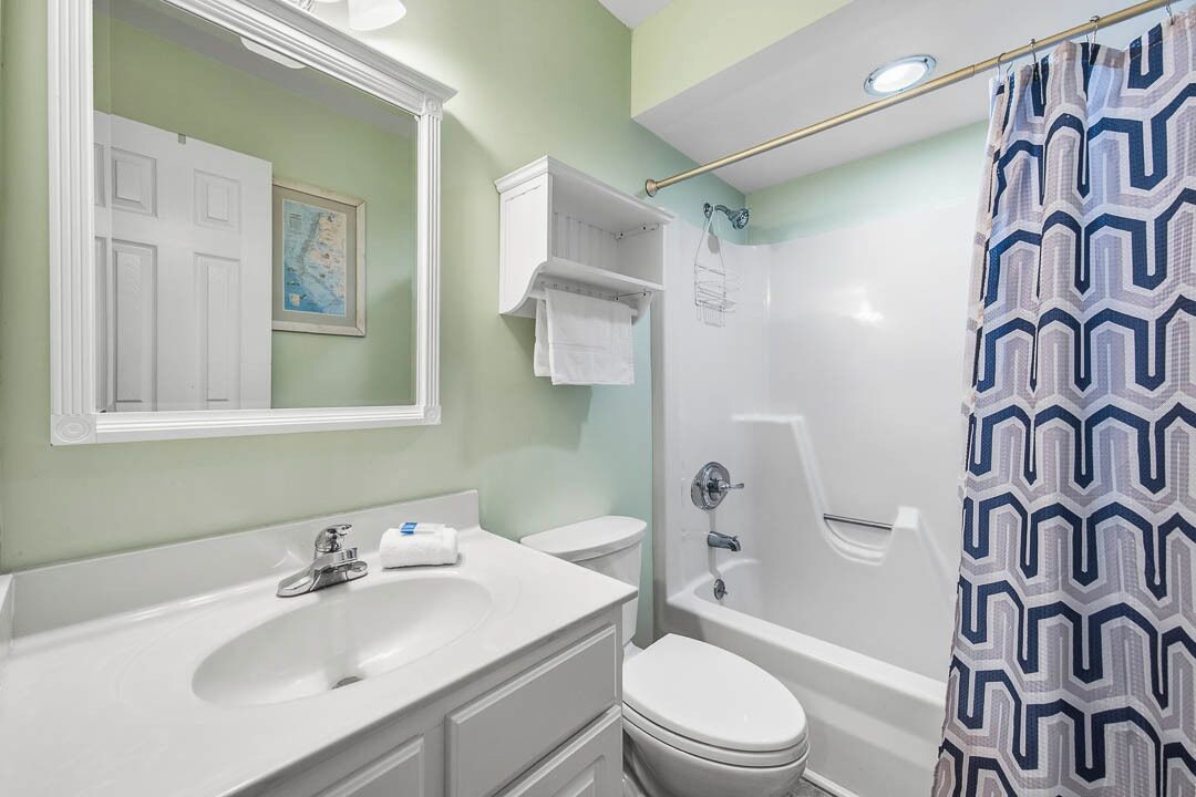 Een badkamer met een wit wastafelmeubel, toilet en bad. Een badgordijn met een geometrisch patroon.