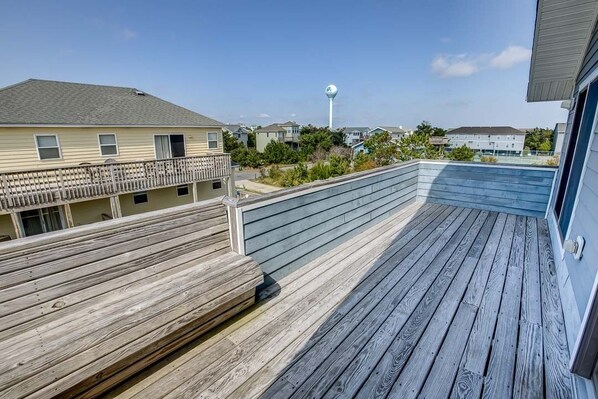 A wooden deck with a railing, overlooking a residential area with houses and a water tower. - Sea Scapes | 817 ft from the beach | Private Pool, Hot Tub | Corolla (Corolla)