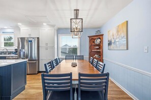 A modern kitchen with white cabinets, a stainless steel refrigerator, and a wooden dining table with chairs.