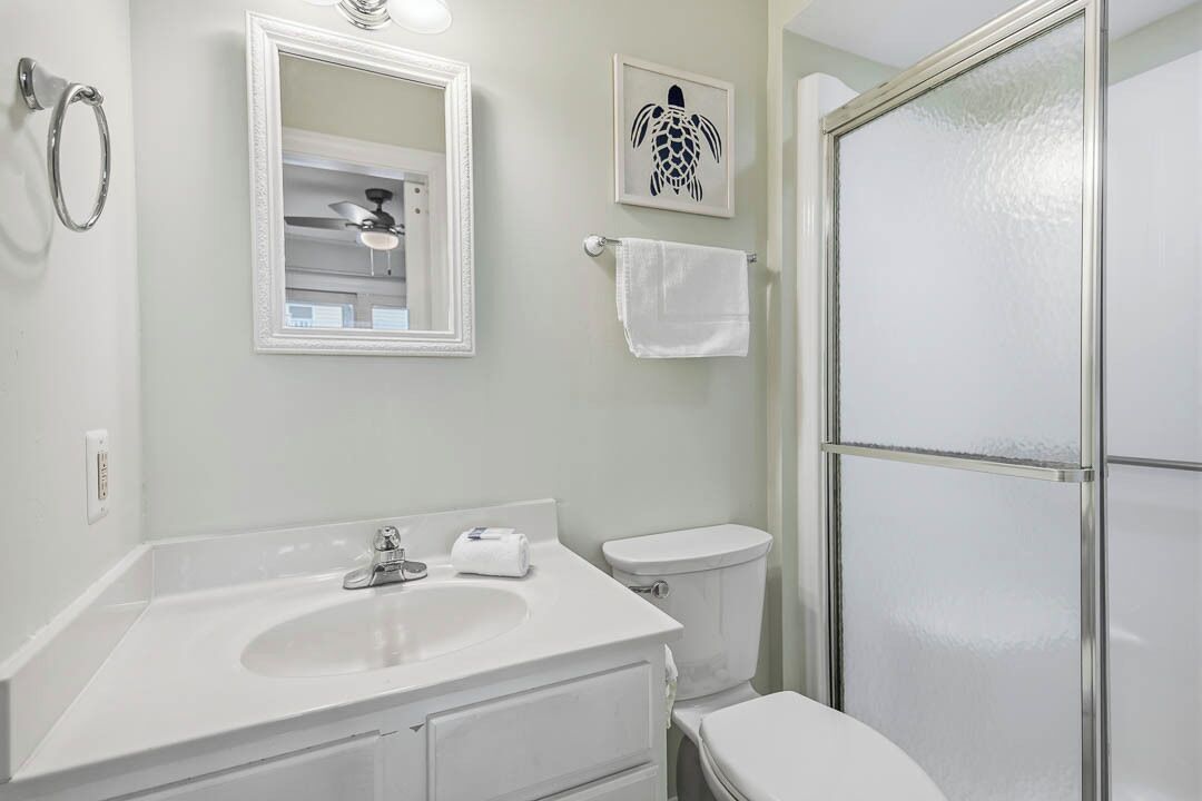 A bathroom with a white sink, mirror, toilet, and a glass shower enclosure.