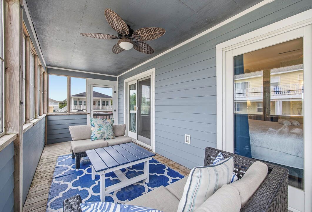 A covered patio with a ceiling fan, a sofa, a table, and a wicker chair.