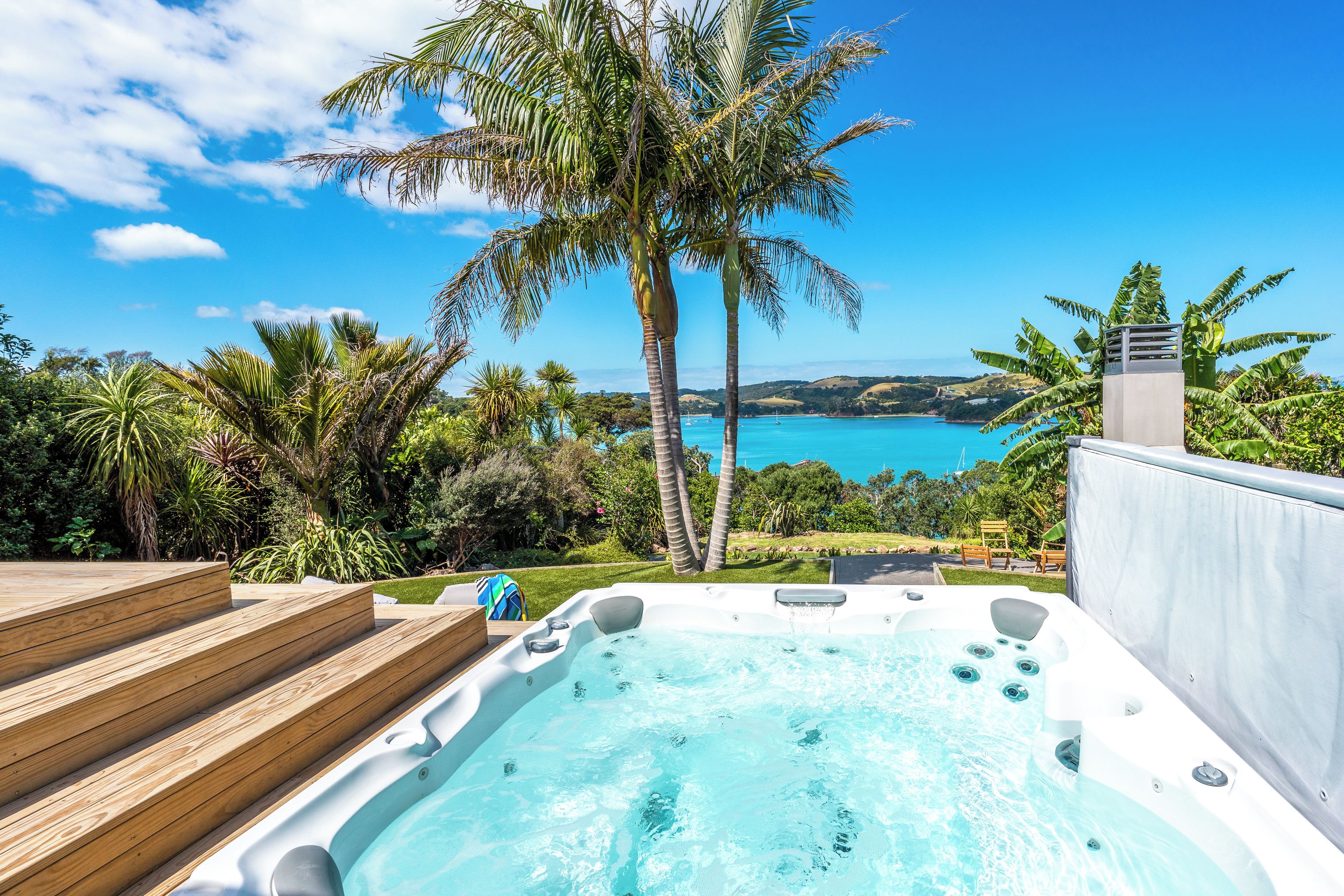 A hot tub with a wooden deck, surrounded by lush greenery and a scenic view of a coastal landscape.